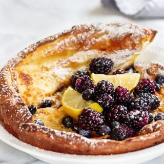 dutch baby pancake in a pie dish topped with black berries and blueberries and powdered sugar.