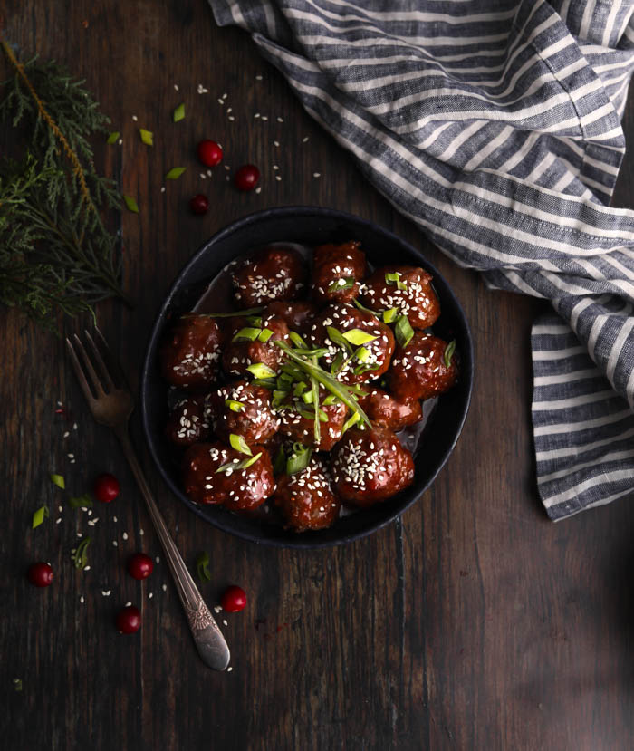 A bowl with cranberry meatballs topped with green onions