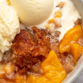 A bowl of ice cream with buttery crisp topping peach cobbler
