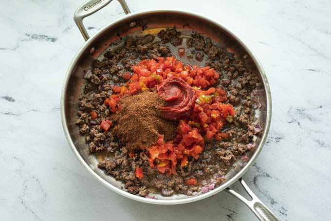 Ingredients for taco pasta in a skillet with ground beef 