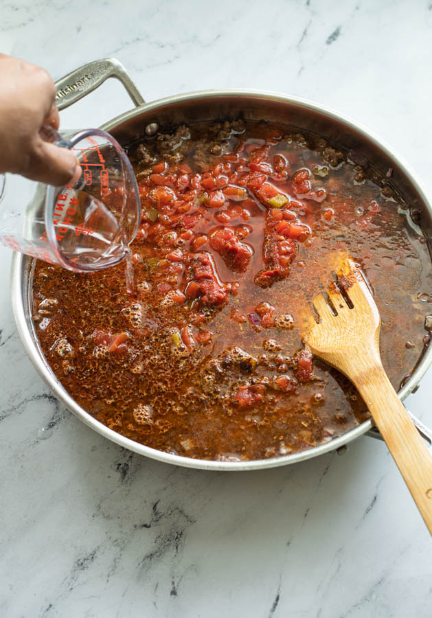 Adding water to a skillet of taco pasta mix 