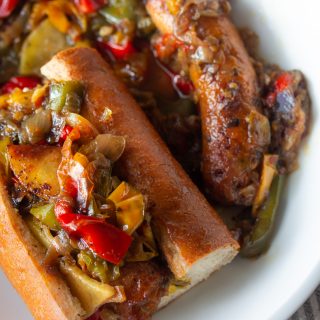 A plate of Italian sausage and peppers on a sub roll