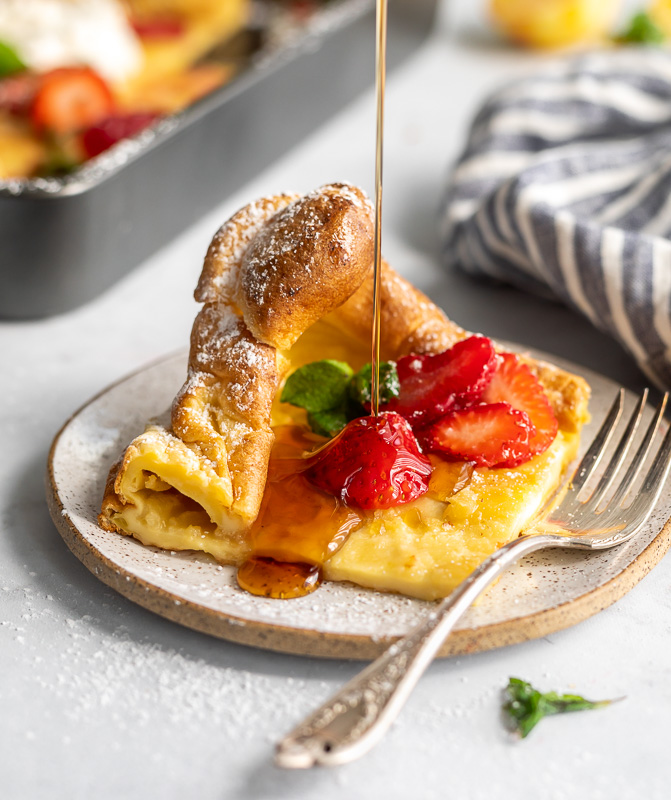 A picture of a slice of a dutch baby pancake on a plate topped with strawberries 