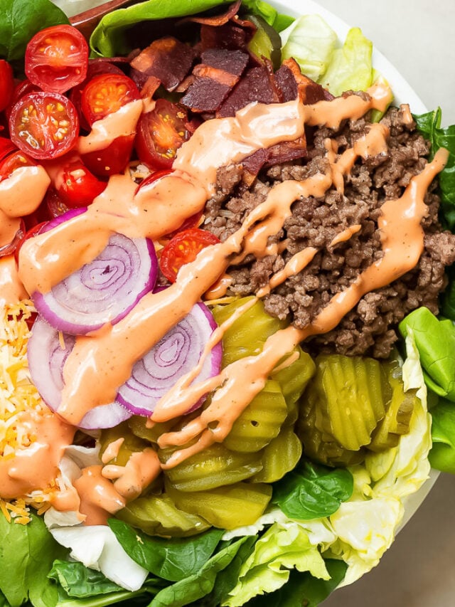 A big mac salad in a bowl with seasoned ground beef, grape tomatoes, red onions, pickles, turkey bacon and shredded cheese with special sauce