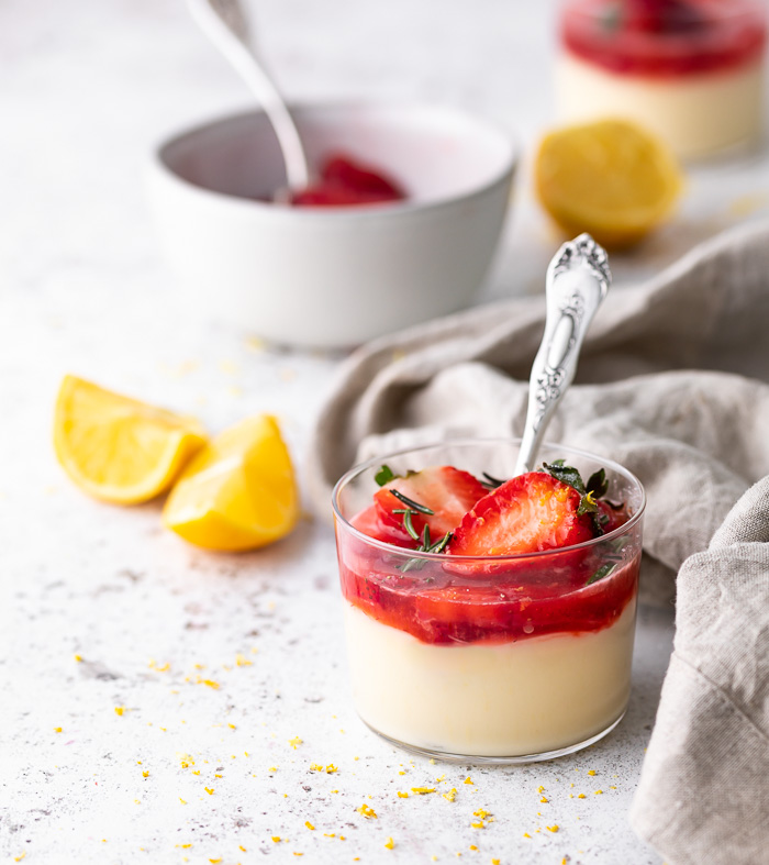 A picture of a dessert glass of lemon posset topped with strawberries 