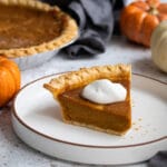 A photo of condensed milk pumpkin pie on a white plate topped with whipped cream