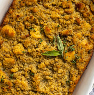 A pan of corn bread dressing topped with sage and thyme garnishment