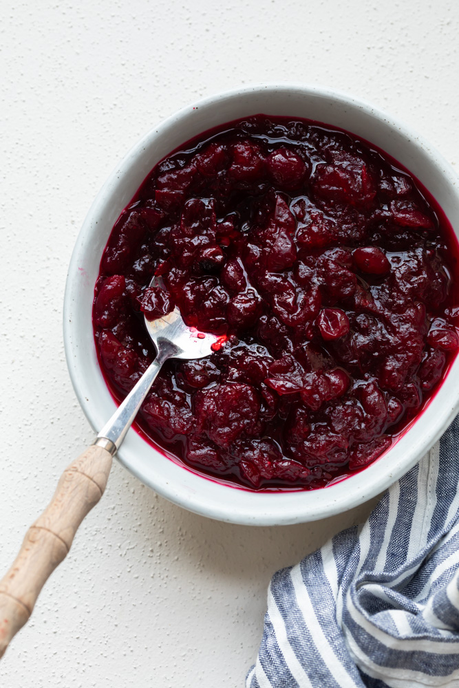A photo of homemade cranberry sauce in a white bowl with a serving spoon 