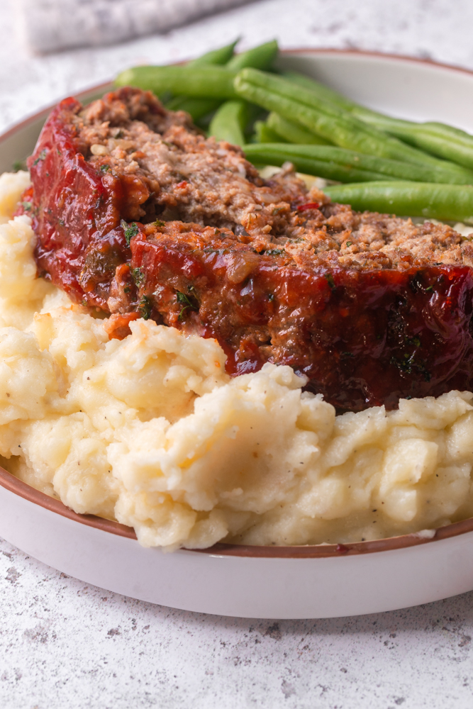 A photo of a thick slice of meatloaf over mashed potatoes on a plate 