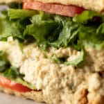 Close-up of a creamy tuna salad sandwich layered with lettuce and tomato on soft sandwich bread.
