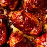 A close-up of a grilled chicken piece generously coated in a thick, glossy rhubarb bbq glaze, served on a white plate with coleslaw and corn on the cob on a marble counter.
