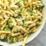 Bowl of creamy chicken broccoli Alfredo pasta with a gold fork lifting a bite of pasta and chicken